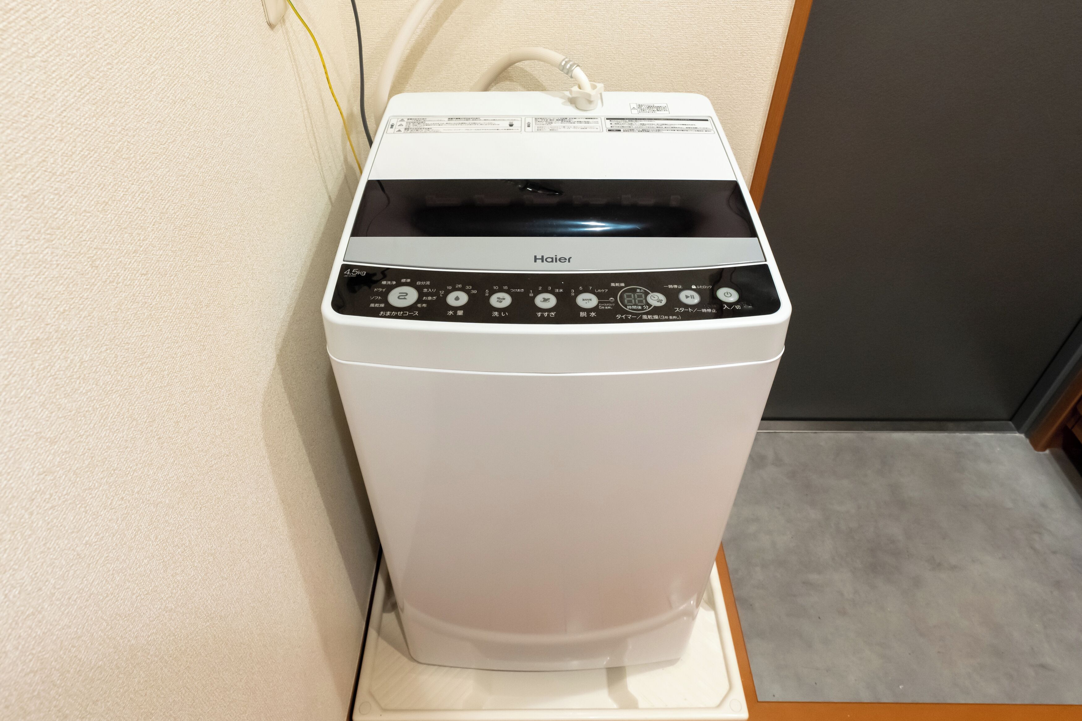 Valkoinen Haier-merkkinen pyykinpesukone, jossa on ohjauspaneeli, virtajohto ja vesiletku.