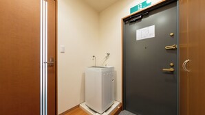 Une pièce avec un plancher en bois, un radiateur blanc, une porte grise dotée d’une poignée et une petite pancarte sur la porte.