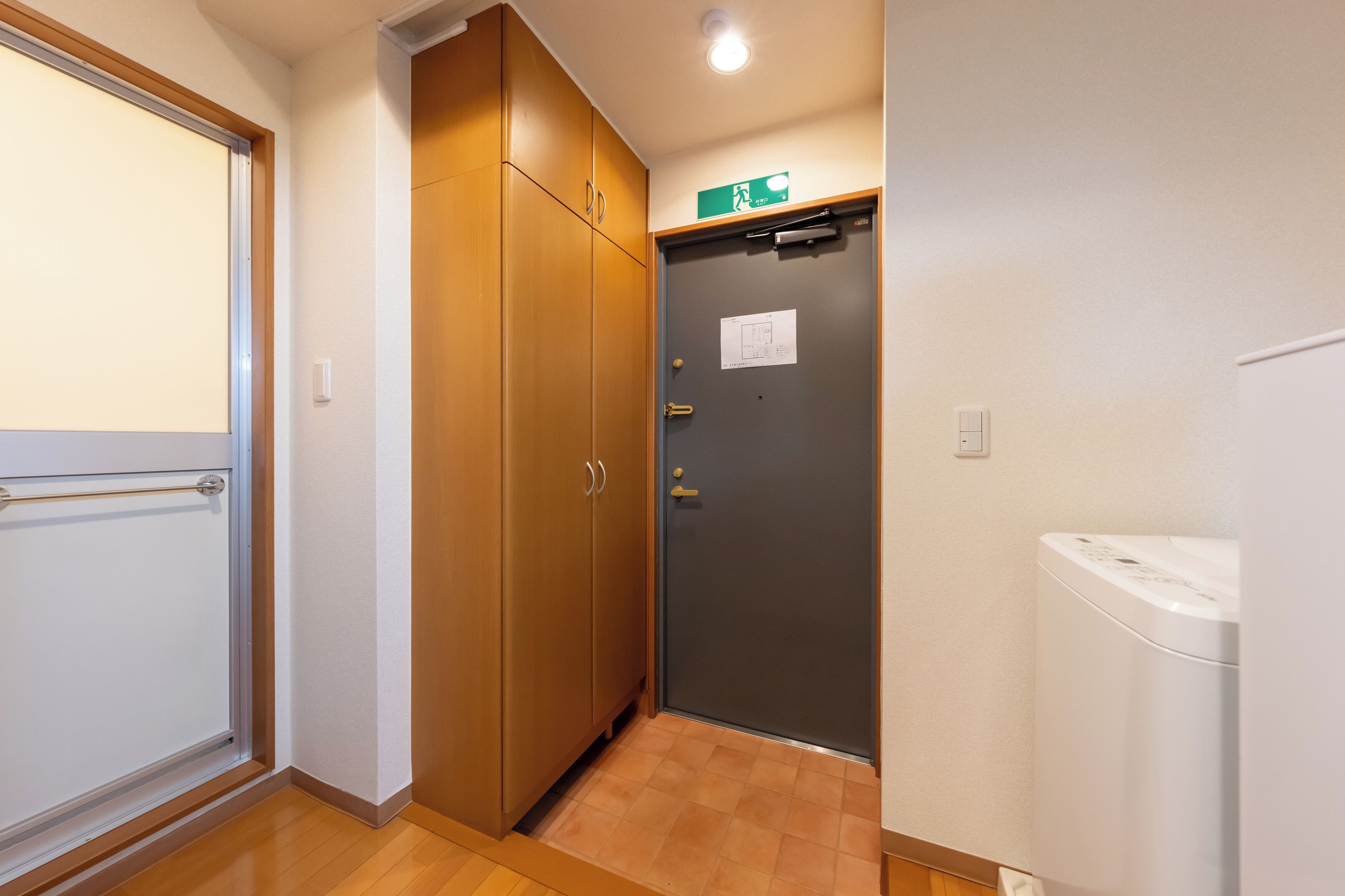Ein Flur mit einem Holzschrank, einer Tür mit einem Notausgangsschild und einer weißen Waschmaschine.