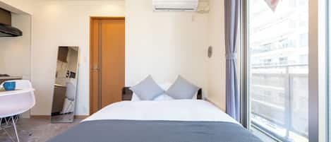 A hotel room with a bed, a desk, a chair, an air conditioning unit, and a window with a view.