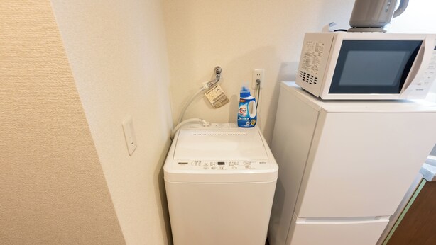 Un lave-linge compact et un four à micro-ondes dans une petite cuisine, le sol étant en bois.