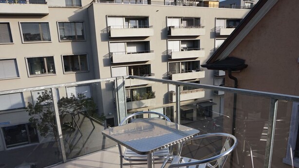 Varanda com mesa e cadeiras, com vista para uma área residencial com vários edifícios.
