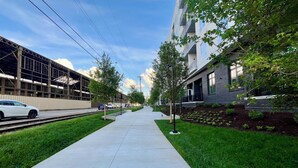 A straight pathway flanked by grass and trees, leading to a modern building with a glass facade. - Riverside Rhythm! Waterfront condo near Broadway, Nissan Stadium, Sounds, etc! (Nashville)