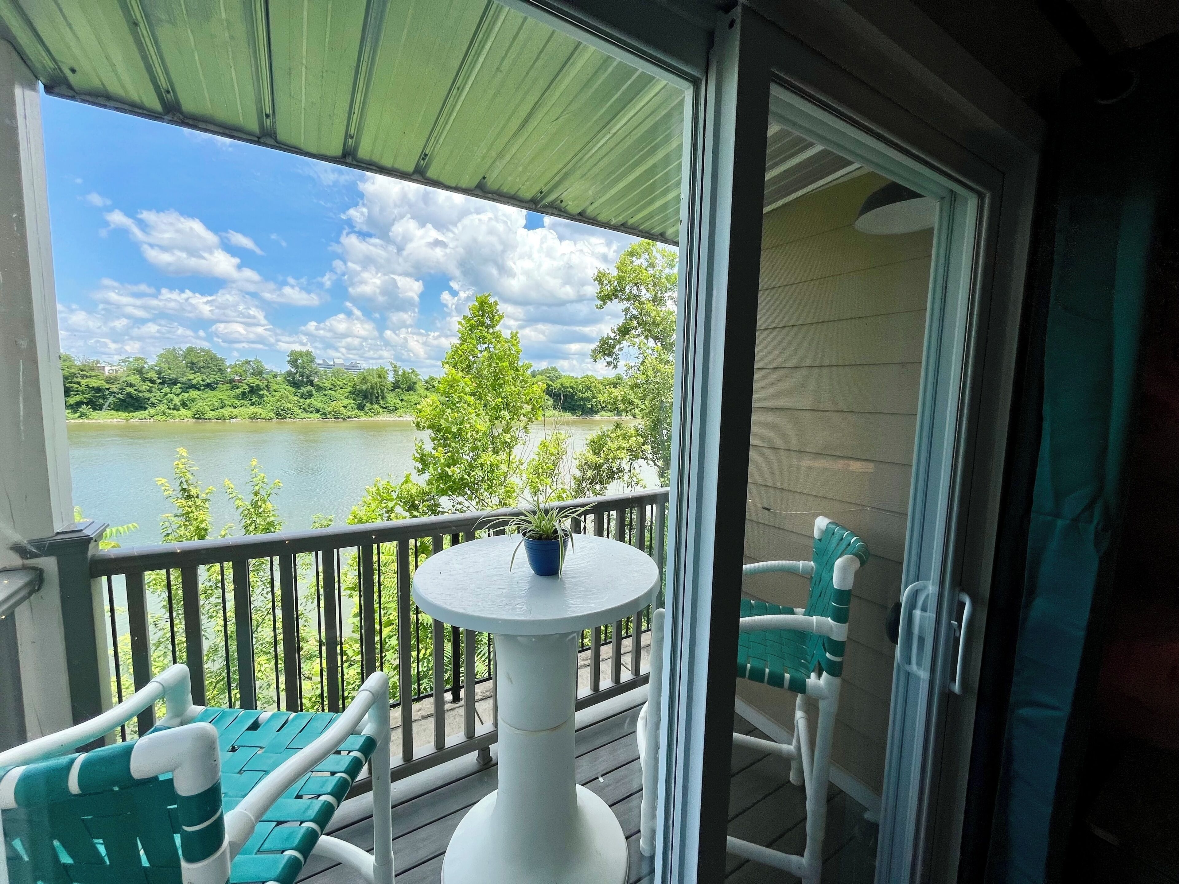 Un balcon avec une table et des chaises, donnant sur un lac bordé d’arbres et sous un ciel dégagé.