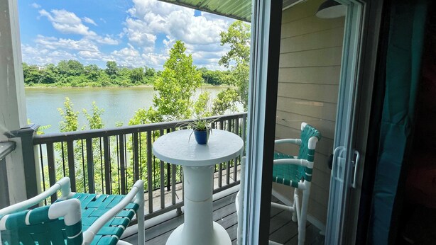 A balcony with a table and chairs, overlooking a lake with trees and a clear sky. - Riverside Rhythm! Waterfront condo near Broadway, Nissan Stadium, Sounds, etc! (Nashville)
