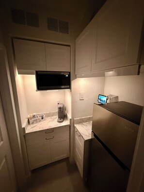 A compact kitchen with a microwave, coffee maker, and a refrigerator.