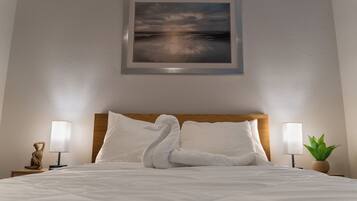 Ein ordentlich bezogenes Bett mit weißer Daunendecke, zwei Kissen und einer dekorativen Schwan-Handtuch-Arrangement. An der Wand über dem Bett hängt ein gerahmtes Landschaftsbild.
