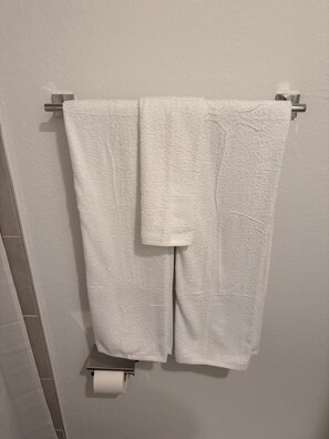 Une serviette blanche est suspendue à un porte-serviettes en métal dans une salle de bain, avec un support à papier toilette en dessous.