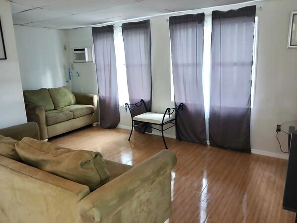 A living room with a sofa, a chair, and a small table. There are curtains on the windows.