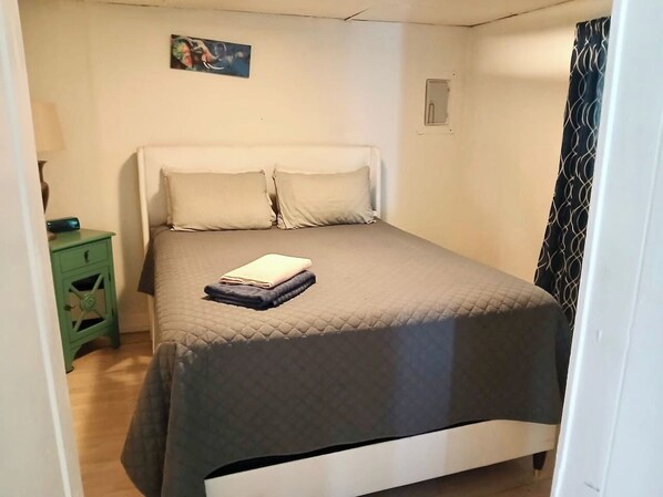 A single bed with a quilted cover, a bedside table with a lamp, and a painting on the wall.