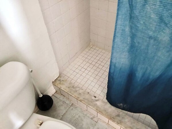 A bathroom with a toilet, a blue shower curtain, and a tiled floor.