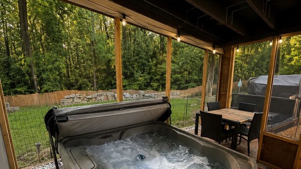 Ein Whirlpool mit Bedienfeld, umgeben von einer Terrassenanlage mit Tisch und Stühlen, mit Blick auf ein bewaldetes Gebiet.