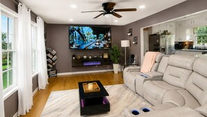 Ein modernes Wohnzimmer mit Flachbildfernseher, Ledersofa, Holzboden und Deckenventilator.