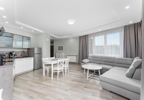 A modern living room with a sofa, a dining table with chairs, a kitchen area with cabinets and appliances, and a large window with curtains. - Rondo Matecznego Harmony Apartment (Kraków)