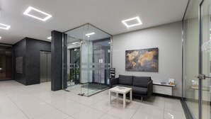 Een moderne lobby met een glazen lift, een witte salontafel, een bank en een kunstwerk van een kaart aan de muur.