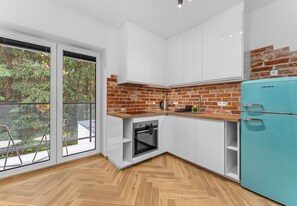 A modern kitchen with white cabinets, a brick accent wall, a built-in oven, and a teal refrigerator.