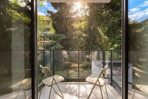 A balcony with two chairs, a glass barrier, and a view of trees and buildings.