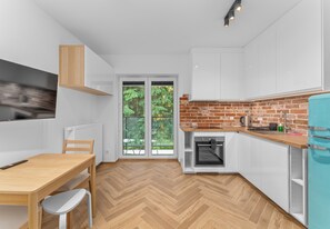 A modern kitchen with white cabinets, a brick backsplash, a wooden table, and a built-in oven.