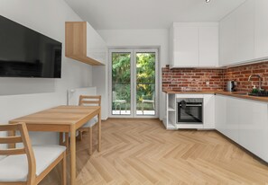 A modern kitchen with white cabinets, a brick backsplash, a built-in oven, and a dining area with a wooden table and chairs. - Rondo Matecznego Studio #23 (Kraków)