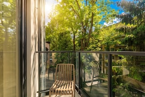 A balcony with a wooden chair, glass railing, and a view of trees and buildings. - Rondo Matecznego Studio #23 (Kraków)