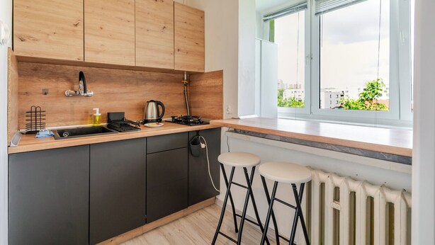 Una cocina moderna con armarios de madera, estufa a gas, hervidor y ventana con vista a edificios.