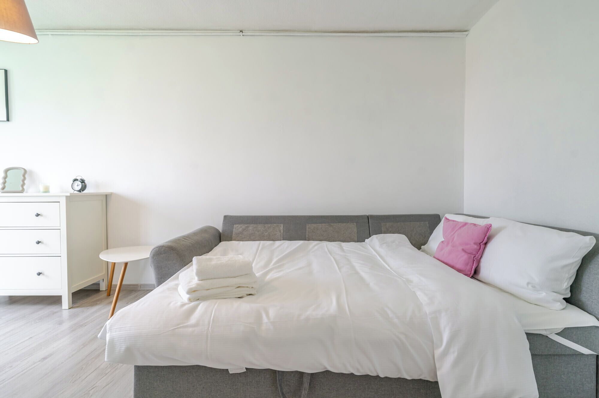 A neatly made bed with a grey headboard, a small bedside table, and a white dresser with drawers.