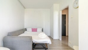 Un dormitorio con una cama, un sofá gris, una mesita y un reloj en la pared.