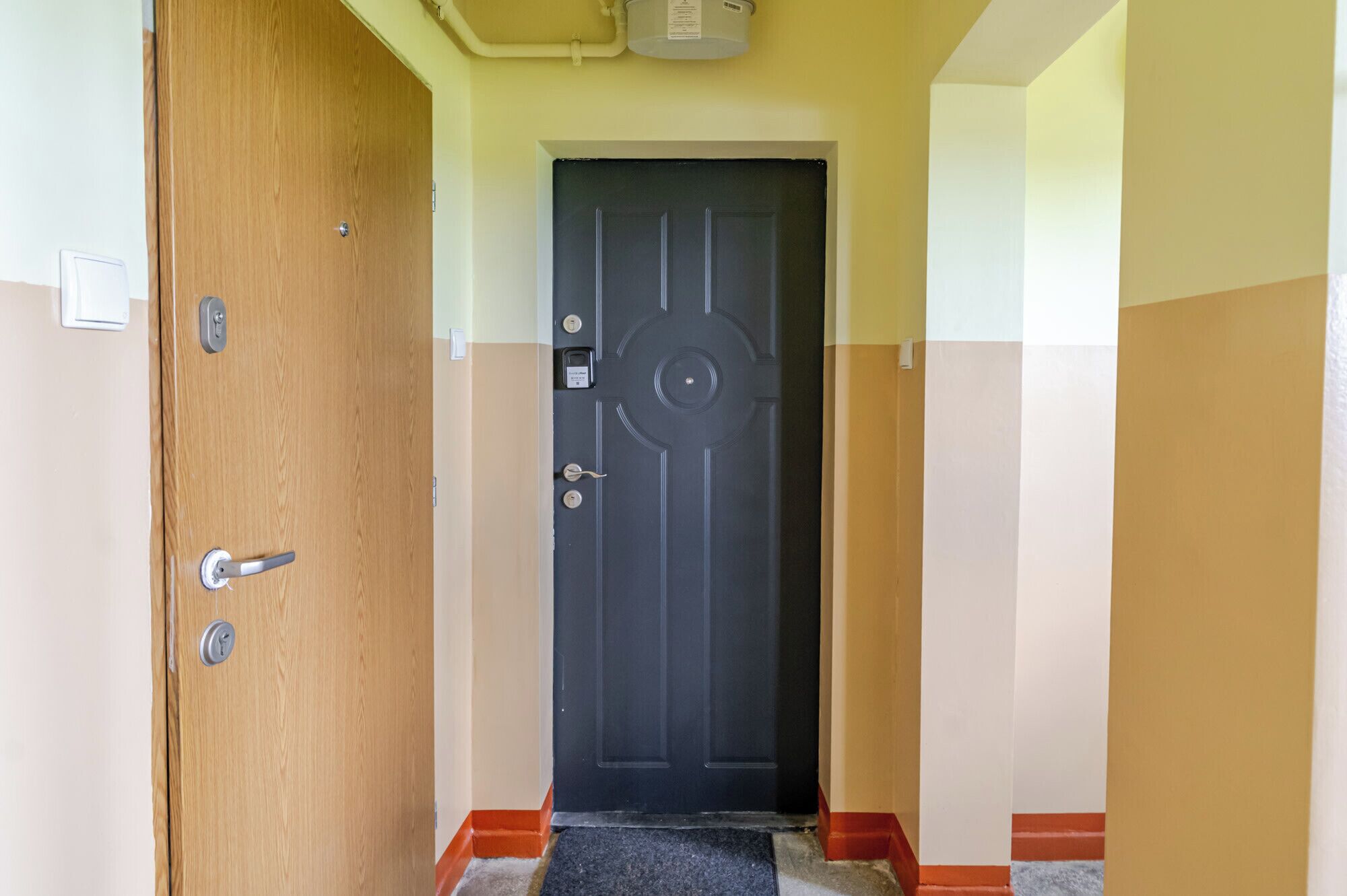 Un pasillo con una puerta de madera, una puerta negra con diseño circular y una pared roja y beige.