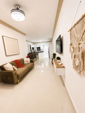 A modern living room with a sofa, a TV, and a macrame wall hanging.