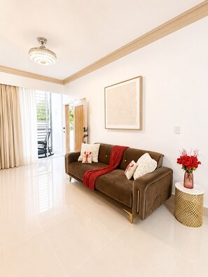 Un salon moderne avec un canapé marron, un plaid rouge et un vase rempli de fleurs rouges posé sur une petite table ronde.