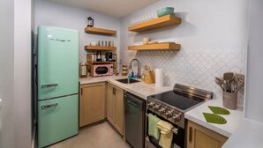 Eine Küche mit einem dunkelblauen, alten Kühlschrank, Holzschränken, einer Mikrowelle und einem Herd.