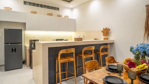 A modern kitchen with a central island, wooden bar stools, and a dining table set for four. - Umalas Jungle Villa (Kerobokan)