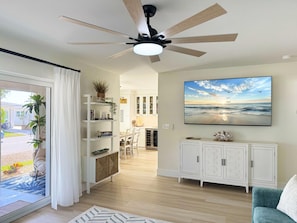 Ein modernes Wohnzimmer mit Deckenventilator, einem großen Fernseher und Blick ins Freie.