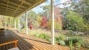 A covered wooden deck with a view of a garden and trees.