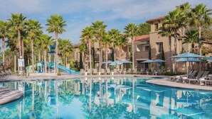 A swimming pool with lounge chairs and umbrellas, surrounded by palm trees and a building with a tiled roof. - 2BR Villa @ Newport Coast Villas ~ Full Resort Access (Newport Beach)