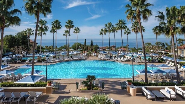 A pool surrounded by palm trees and lounge chairs, with a clear view of the ocean. - 2BR Villa @ Newport Coast Villas ~ Full Resort Access (Newport Beach)
