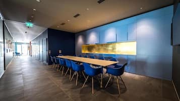 A modern conference room with a long table, blue chairs, and a large abstract painting on the wall.