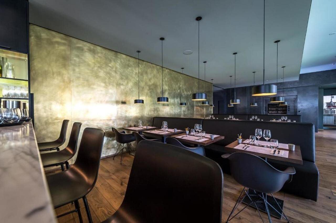 A modern restaurant interior with a bar area, dining tables, and black chairs.