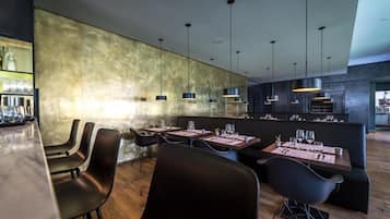 A modern restaurant interior with a bar area, dining tables, and black chairs.