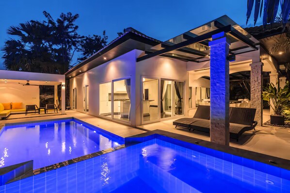 Una casa moderna con piscina, puertas de cristal y mobiliario de exterior.