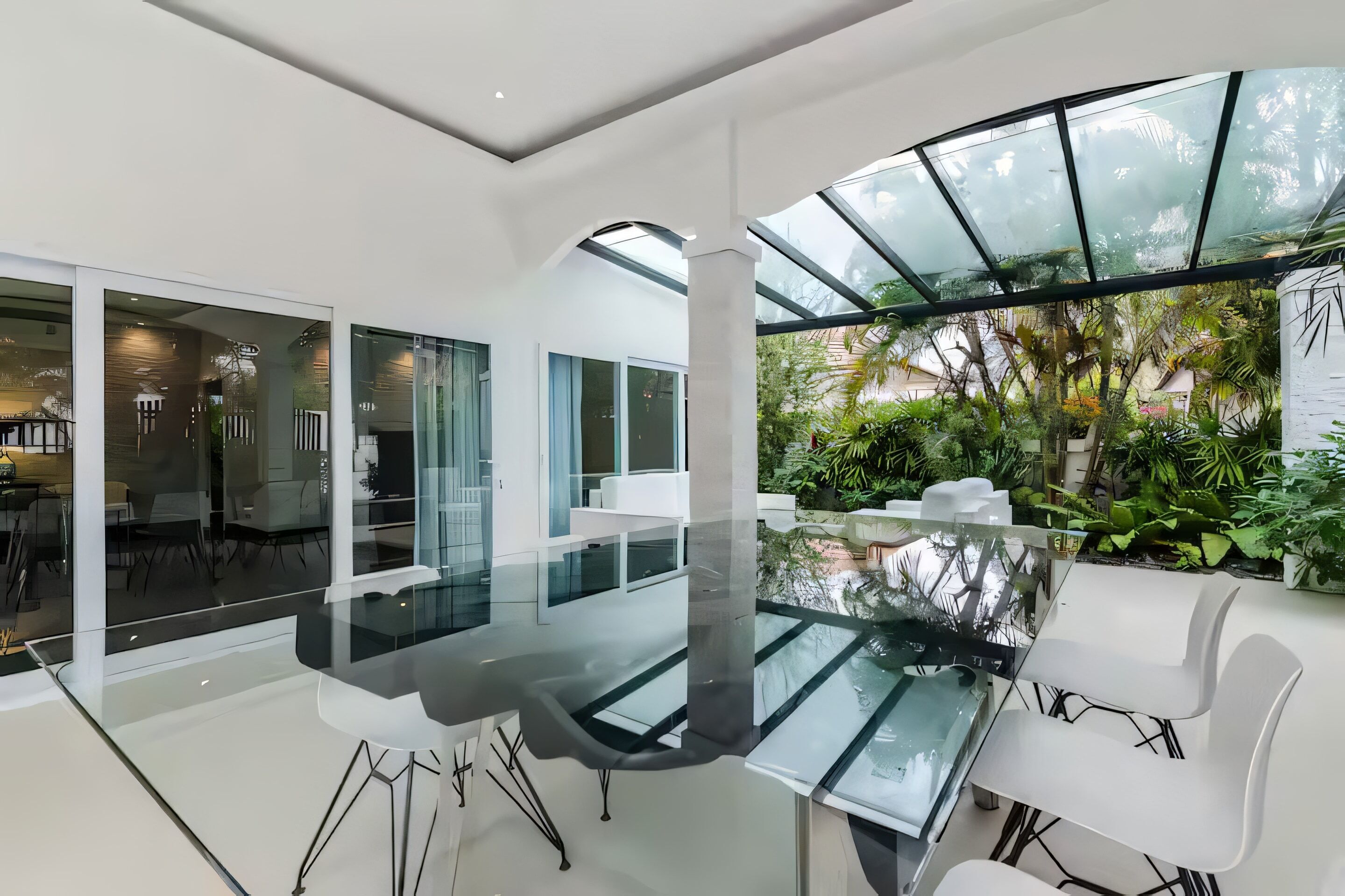 A modern interior with a glass table, white chairs, and a glass ceiling allowing natural light.