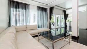 A modern living room with a glass coffee table, a beige sofa, and large windows with curtains. - Orchid Paradise Homes OPV03 (Hin Lek Fai)