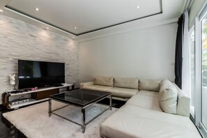 Una sala de estar moderna con un televisor de pantalla plana, una mesa de centro de vidrio, un sofá color beige y una alfombra blanca.