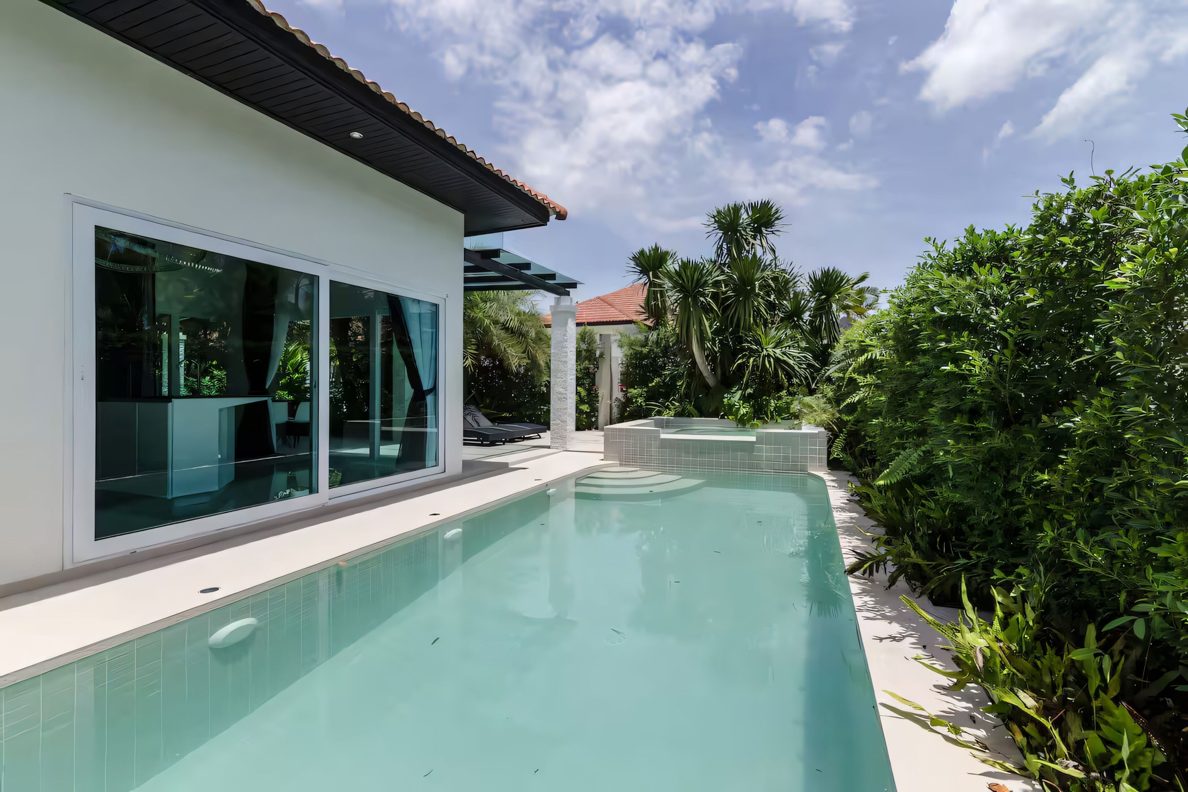 A swimming pool with a modern house, large windows, and lush greenery.