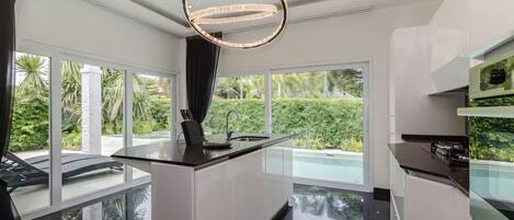 A modern kitchen with a central island, large windows, and a chandelier.