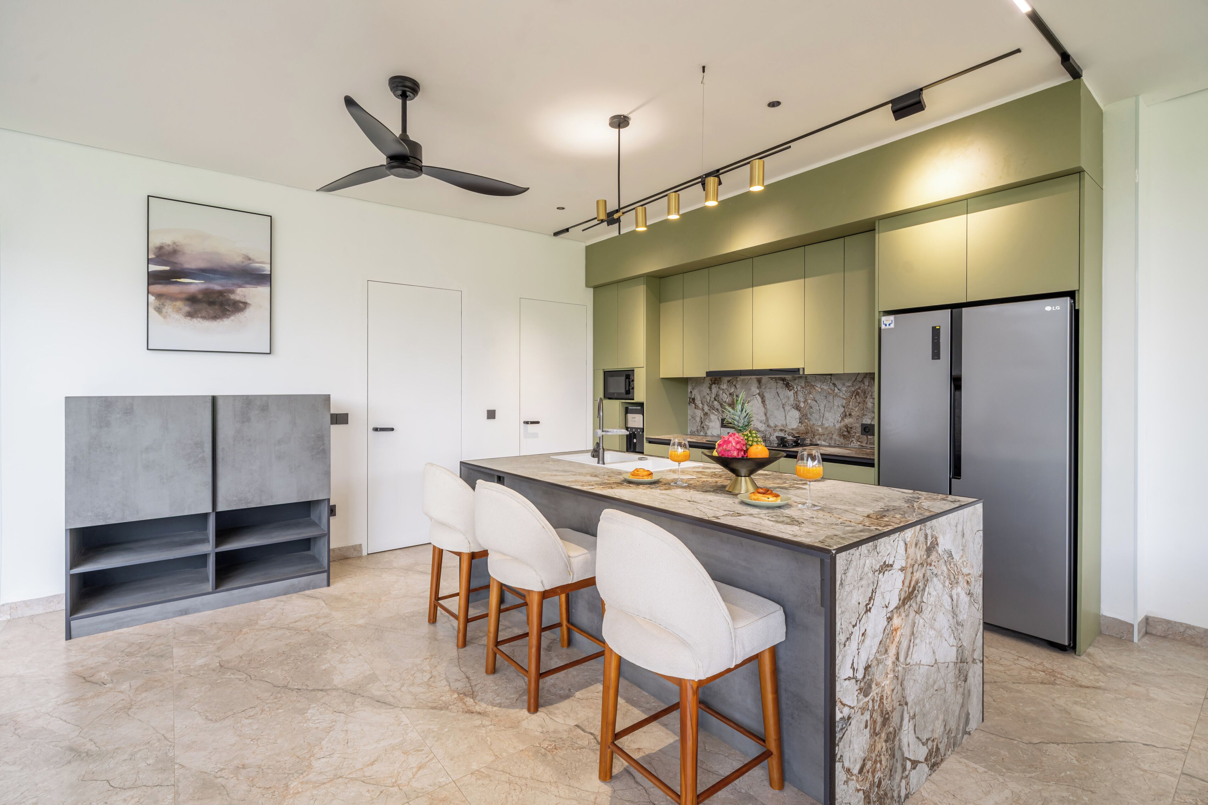 Una cocina moderna con una isla de mármol, taburetes de bar, horno empotrado y refrigerador de acero inoxidable.