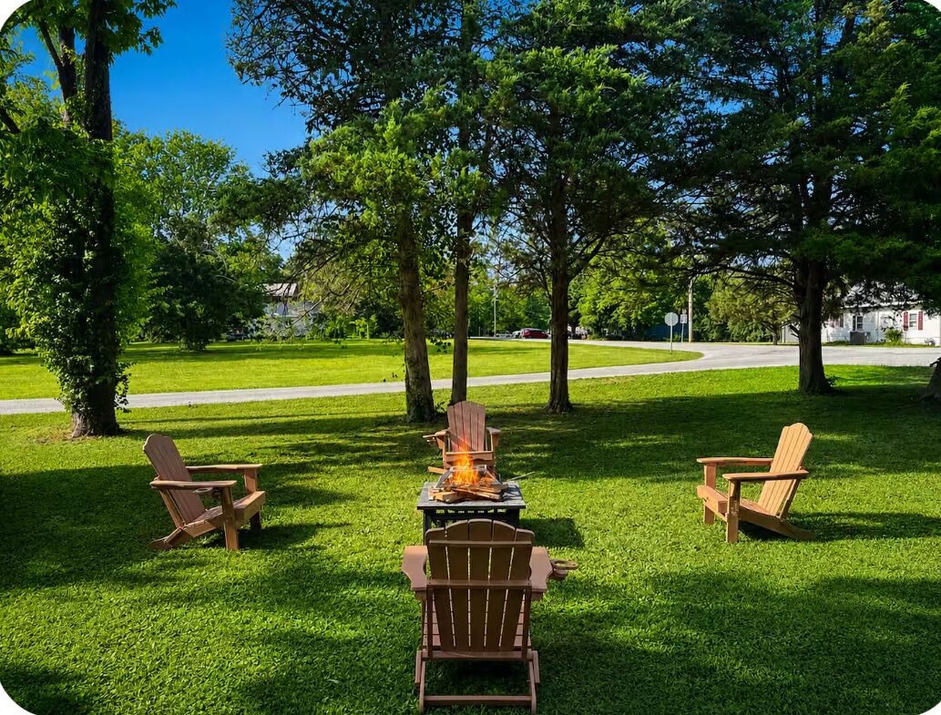 A grassy outdoor area with a fire pit and three Adirondack chairs.