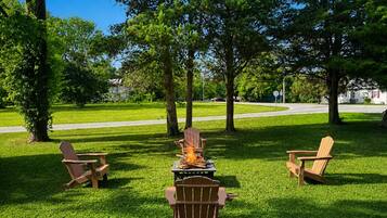 A grassy outdoor area with a fire pit and three Adirondack chairs.
