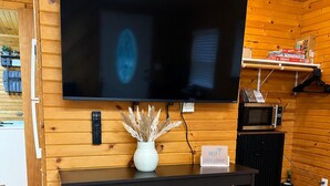 Ett rum med träpanel på väggarna, en platt-TV som hänger på väggen, ett svart konsolbord med dekorativa föremål och en mikrovågsugn som står på en hylla.