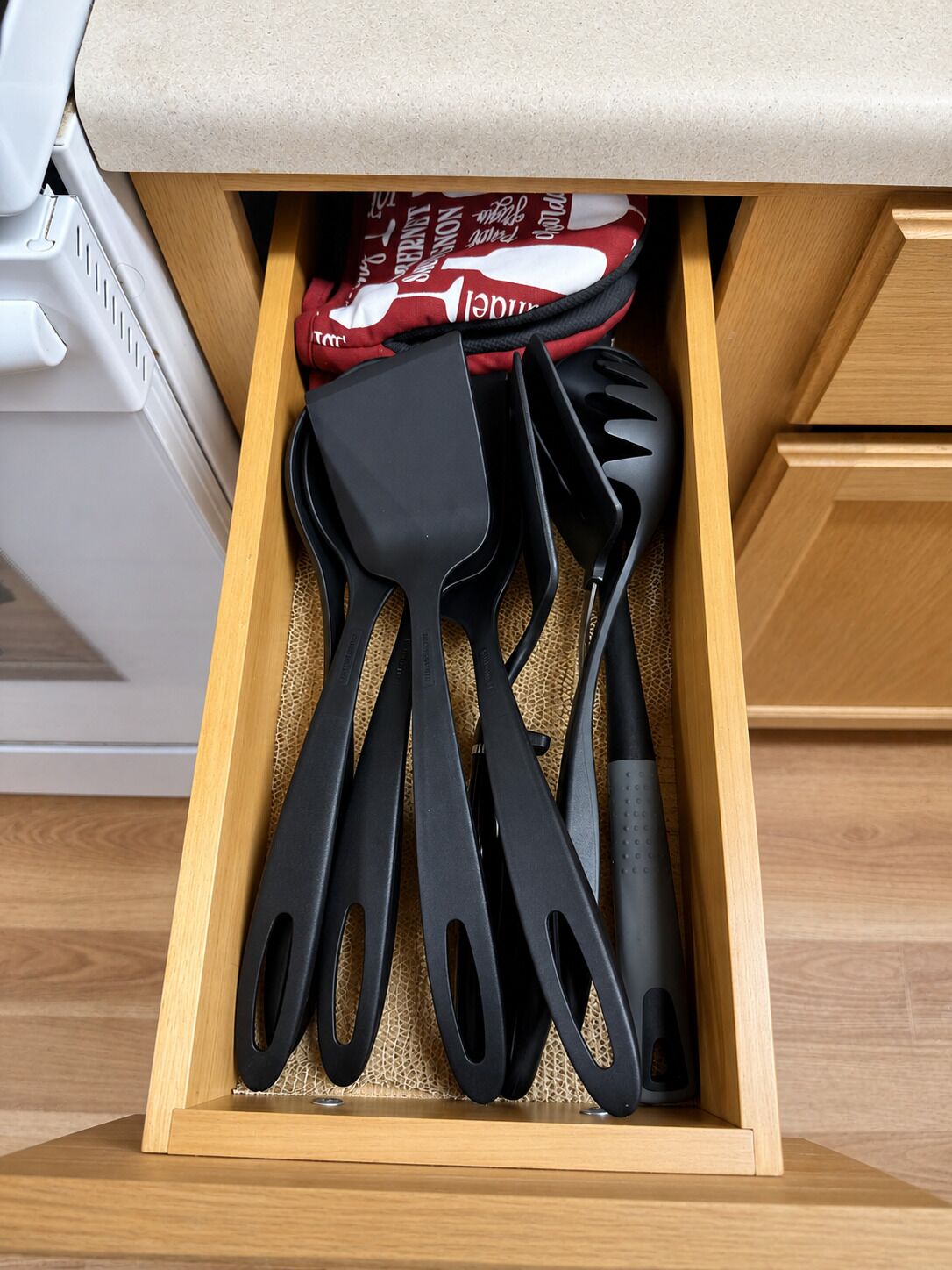 Un tiroir contenant des ustensiles de cuisine noirs, un sac rouge et blanc, et un meuble en bois.
